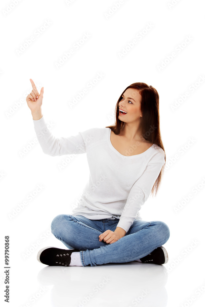 Young smiling woman sitting on the floor and pointing up Young smiling woman sitting on the floor and pointing up