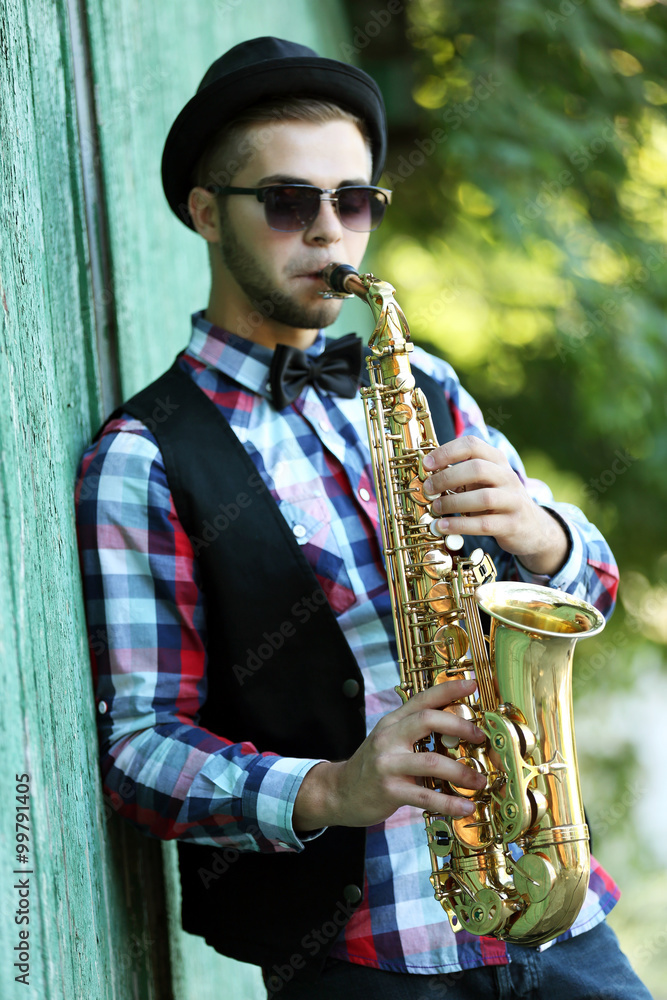 Fototapeta premium Young man playing on saxophone outside near the old wall