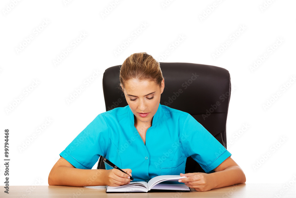 Female doctor sitting behind the desk and writing a notes Female doctor sitting behind the desk and writing a notes