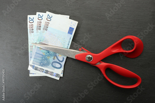 Red scissors cut money on black background. Financial concept