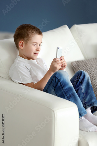 Little boy using mobile phone on a sofa at home