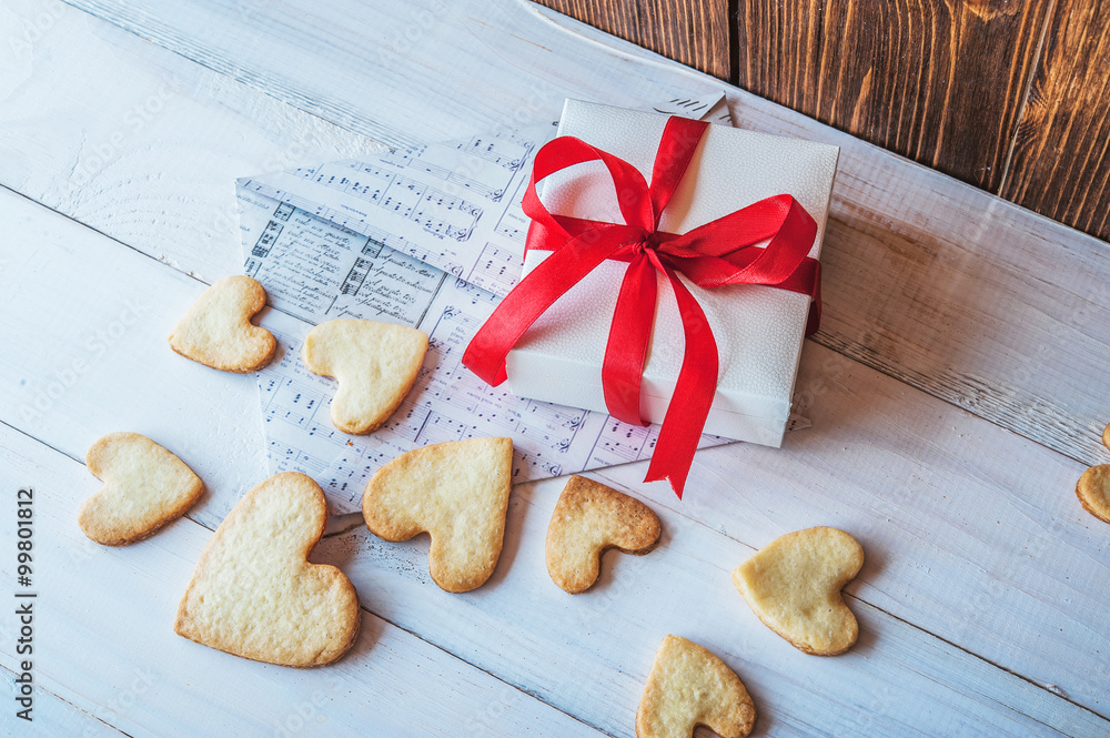 White box with red ribbon, the envelope, cookies in the shape of heart, red candles. Romantic gift on Valentine's Day on wooden background. White box with red ribbon, the envelope, cookies in the shape of heart, red candles. Romantic gift on Valentine's Day on wooden background.