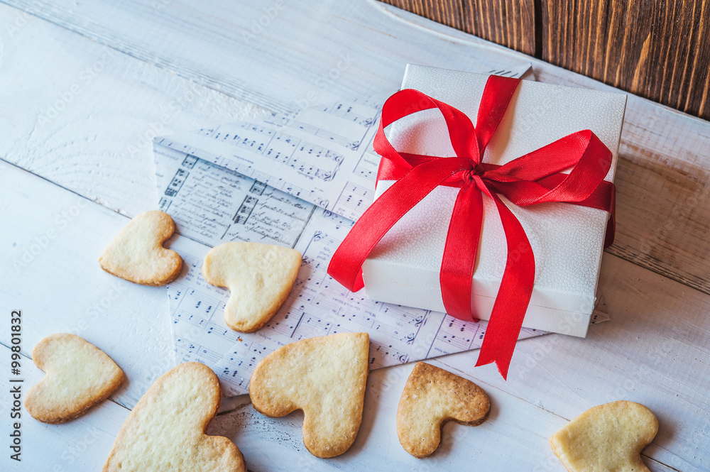 White box with red ribbon, the envelope, cookies in the shape of heart, red candles. Romantic gift on Valentine's Day on wooden background. White box with red ribbon, the envelope, cookies in the shape of heart, red candles. Romantic gift on Valentine's Day on wooden background.