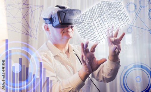 the silver-haired man getting experience using VR-headset glasses of virtual reality presses imaginary interactive monitor on the background of the graphs and charts