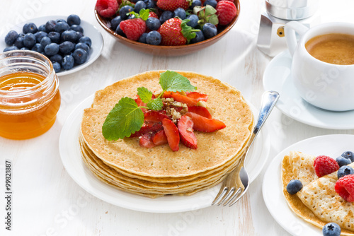 crepes with strawberry, jams and honey on white table, close-up