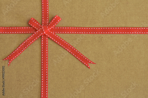 Red ribbon bow on recycled card as background photo