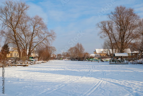 Rural winter landscape with frozen river and houses on the riverbank