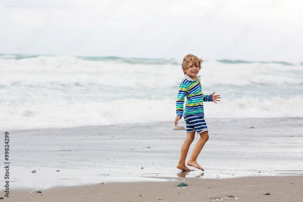 Little kid boy playing on beach on stormy day