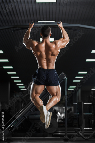 Muscle athlete man in gym making elevations. Bodybuilder training pull ups on horizontal bar