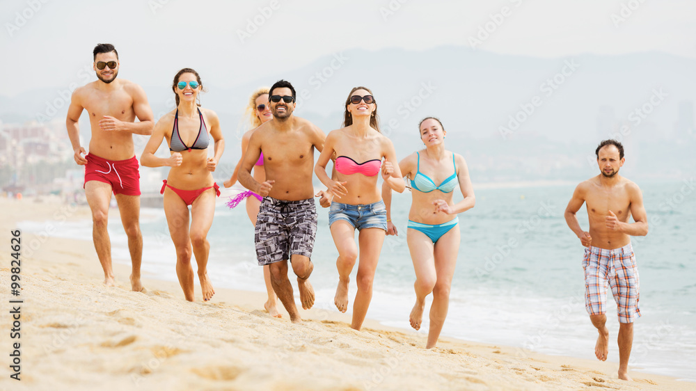 Smiling adults friends running at beach