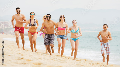 Smiling adults friends running at beach