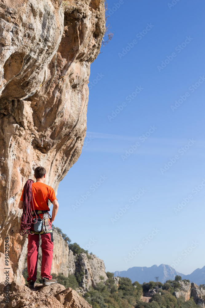 Fototapeta premium Young man climbing on a limestone wall with wide valley on the background