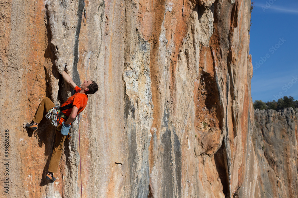 Fototapeta premium Young man climbing on a limestone wall with wide valley on the background