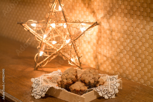 Muffins with apples and cinnamon on wood table near Christmas light.