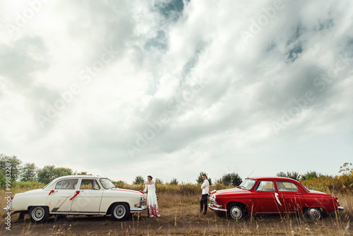 stylish bride and happy groom near two retro cars on the backgr