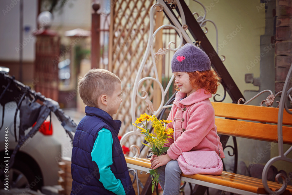 Funny kids, happy little boy giving a cute girl bouquet of yello