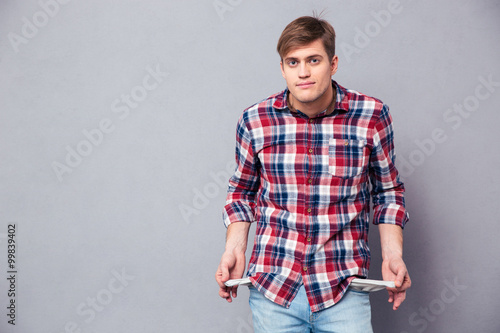 Poor handsome young man in checkered shirt showing empty pockets