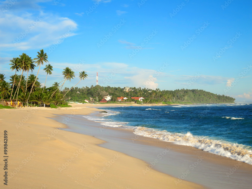 Empty tropical beach with white sand, palm trees and turquoise ocean under blue sky