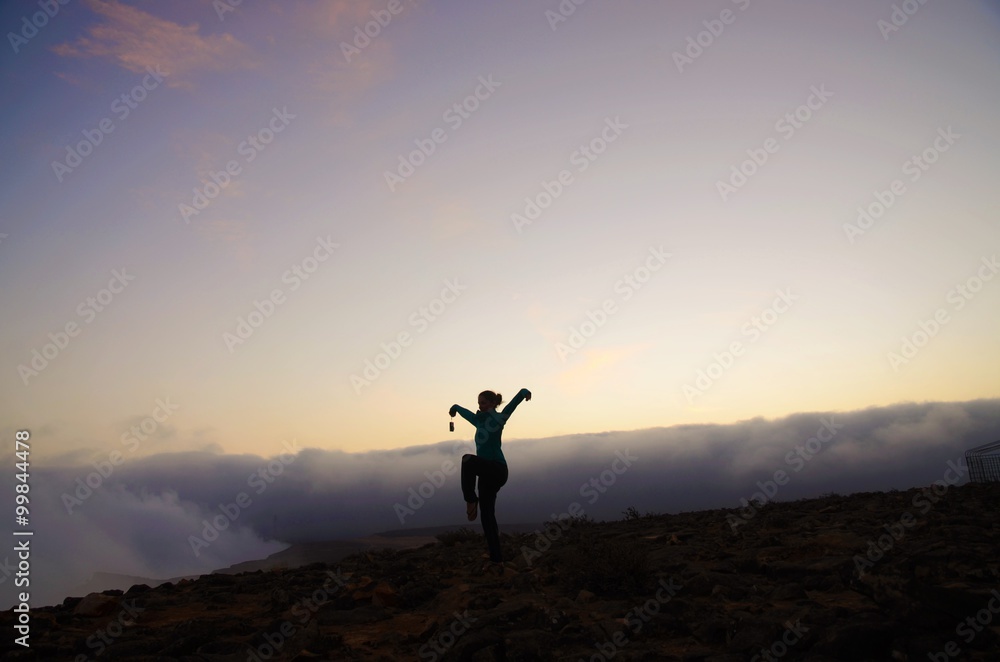 Woman in the crane position on top of a mountain in Oman during sunset