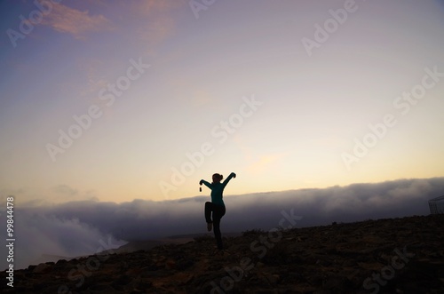 Woman in the crane position on top of a mountain in Oman during sunset