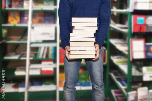 uomo in libreria che acquista libri tenendoli in mano tra corridoio e scaffali photo