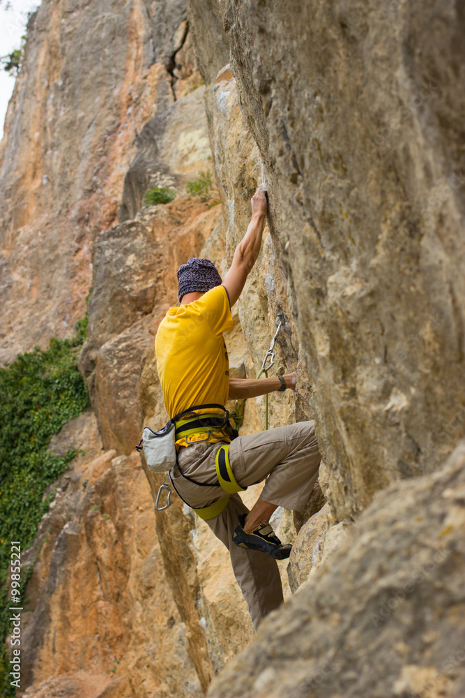 Young male climber hanging by a cliff.