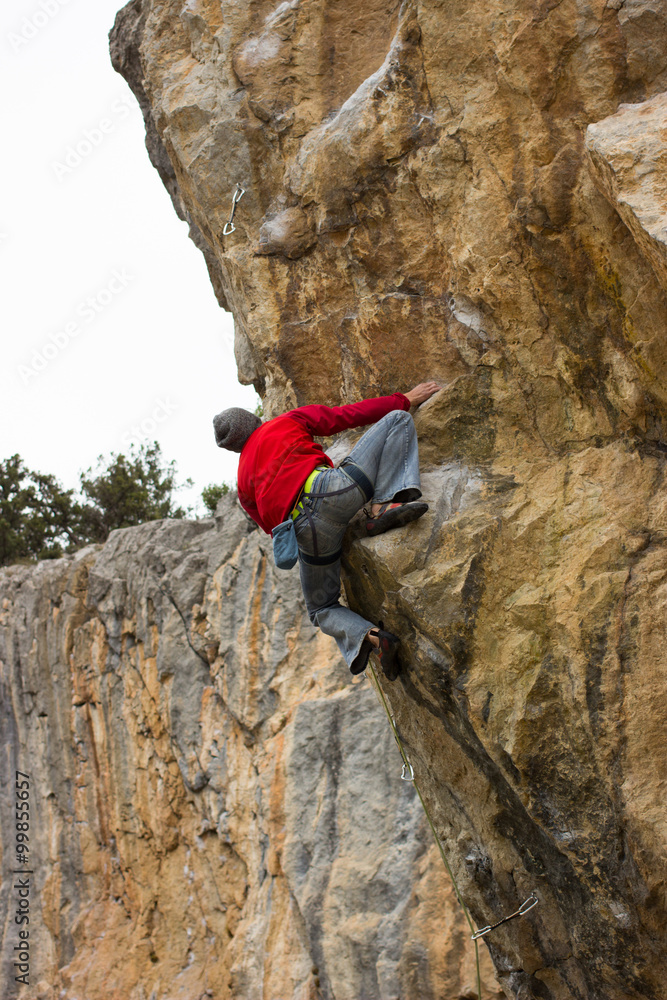 Young male climber hanging on a cliff with a rope.