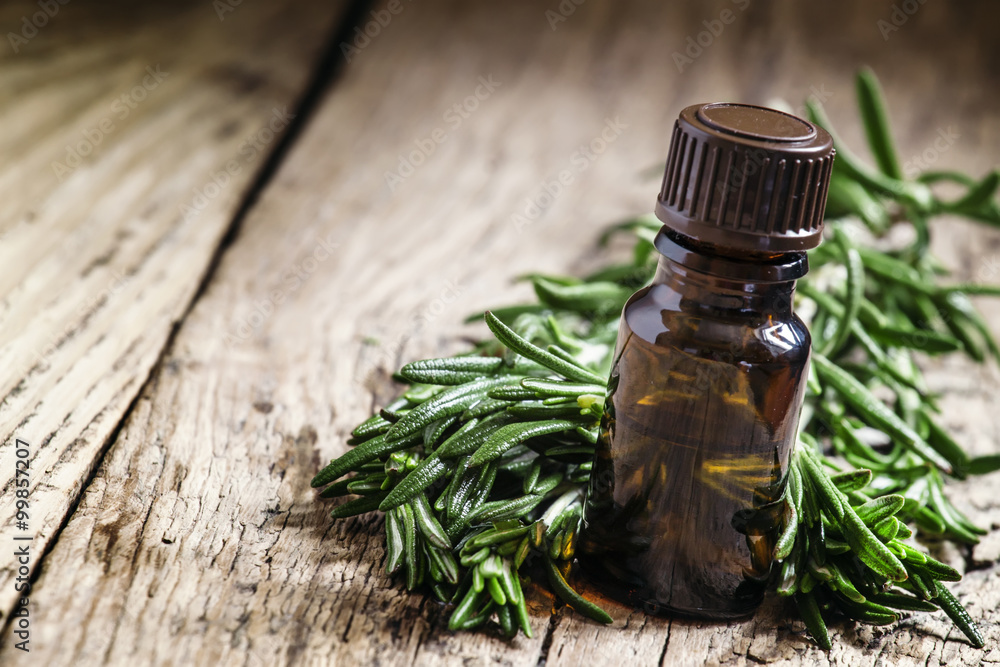 Rosemary essential oil in a small bottle and fresh rosemary on a Rosemary essential oil in a small bottle and fresh rosemary on a