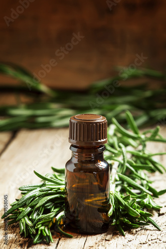 Rosemary essential oil in a small bottle and fresh rosemary on a