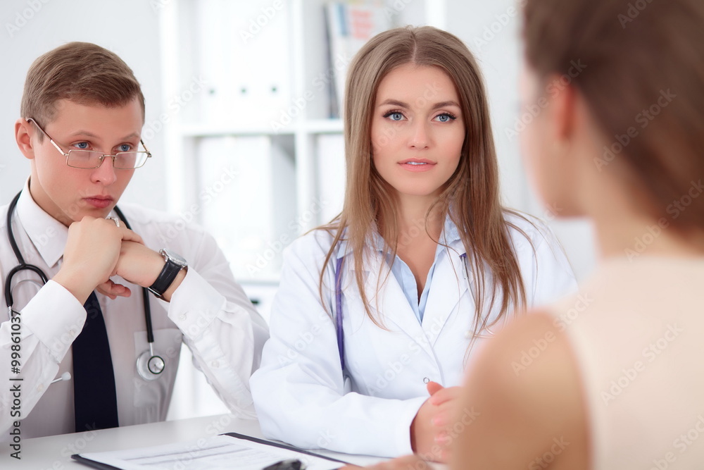 Two confident friendly doctors sitting at the table and listen to the patient's history . Medical and health care concept Two confident friendly doctors sitting at the table and listen to the patient's history . Medical and health care concept