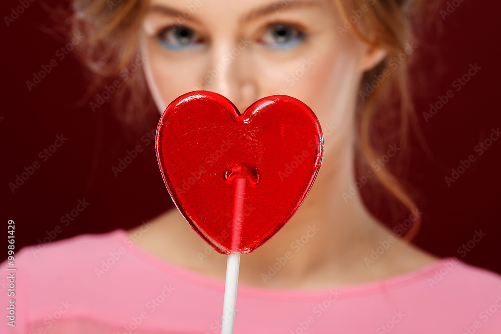 Valentine's Day. Young girl with red heart on red background.red heart in focus Valentine's Day. Young girl with red heart on red background.red heart in focus