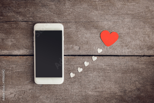 Smartphone and hearts paper on wooden background