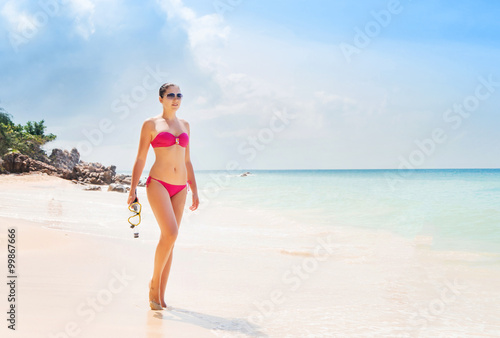 Beautiful, young lady in pink swimwear posing on the beach with diving mask.