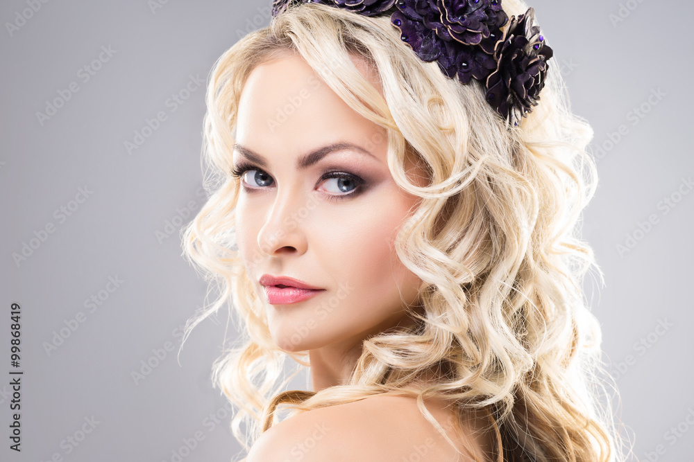 Close-up of absolutely gorgeous model with pure skin and bare shoulders wearing purple flower alike crown over grey background.