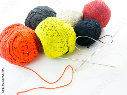 multi color balls of wool and knitting needles over white background