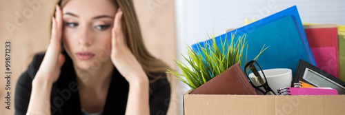 Young dismissed female worker sitting near the carton box with h