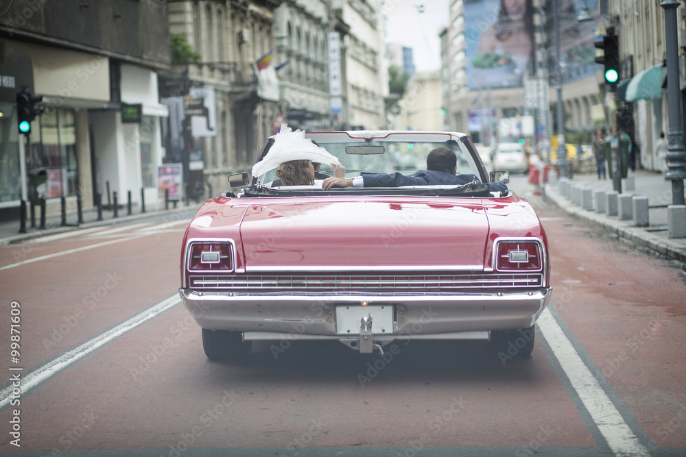 A newlywed married couple is driving a convertible retro car in A newlywed married couple is driving a convertible retro car in