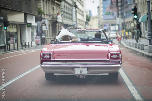 A newlywed married couple is driving a convertible retro car in photo