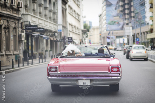 A newlywed married couple is driving a convertible retro car in © danmir12