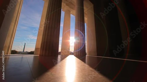 Lincoln Memorial, tracking shot of giant pillars with lens flare and blue cloudy sky, early morning.