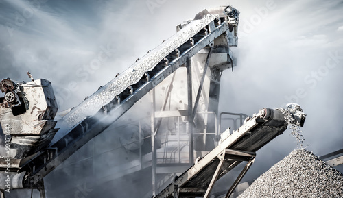 Cement production factory on mining quarry. Conveyor belt of heavy machinery loads stones and gravel photo
