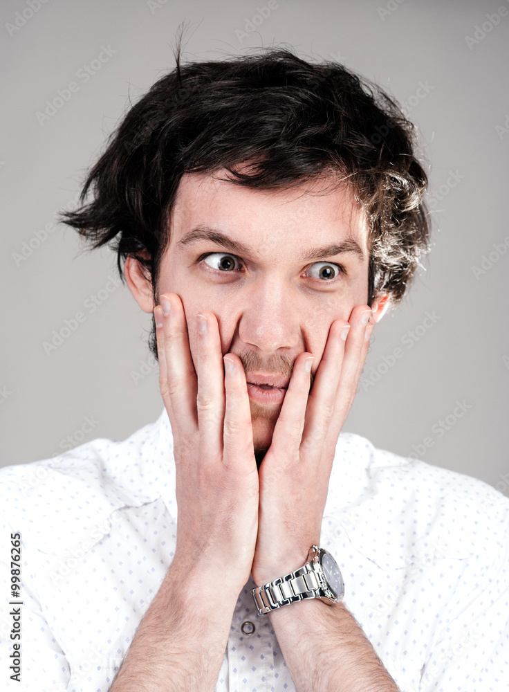 Young man looking surprised with his arms on the face. Light background. Messy hairdo. Young man looking surprised with his arms on the face. Light background. Messy hairdo.
