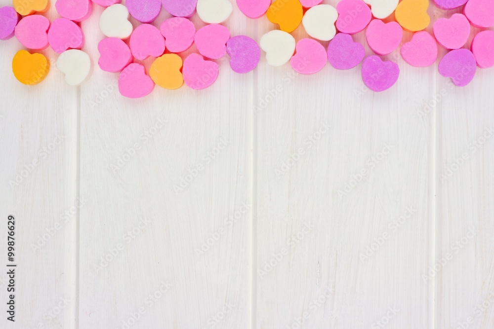 Valentines Day sugar candy hearts forming a top border over a white wood background