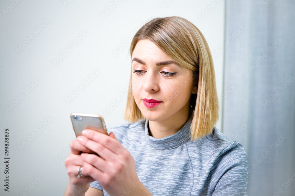 Young pretty business woman with mobile phone sitting at her workplace in office