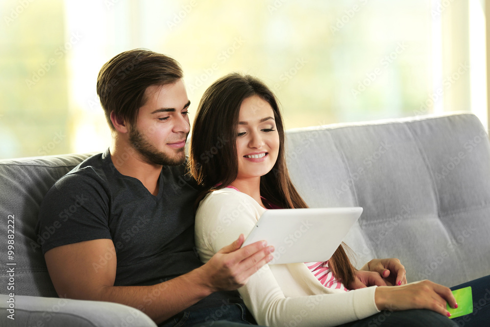 Young happy couple using credit card with tablet at home on light background Young happy couple using credit card with tablet at home on light background