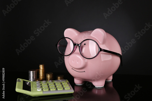 Piggy bank in glasses with calculator and coins on dark background