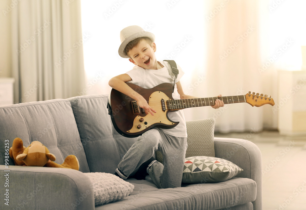 Obraz premium Little boy playing guitar on a sofa at home