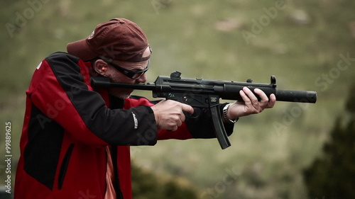 Man in baseball cap and red jacket shooting an MP5 photo