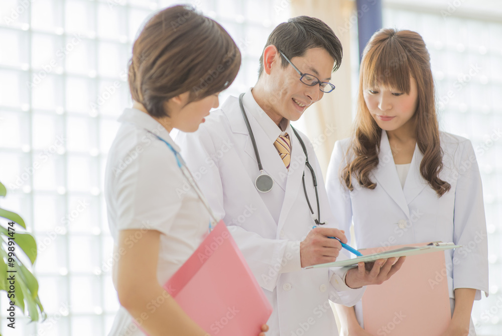 Fototapeta premium 病院内で書類を見る男性医師・女性医師と女性看護師