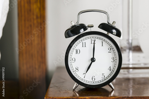 Black alarm clock showing 7 o'clock on bedside table